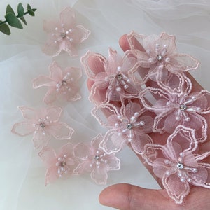 May include: A collection of delicate pink floral appliques with pearl and rhinestone embellishments. These lace appliques are perfect for adding a touch of elegance to wedding dresses, bridal accessories, or other craft projects.