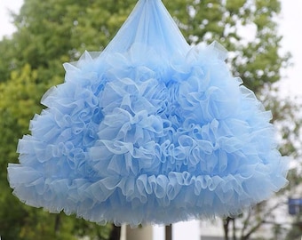 May include: A light blue tulle skirt with multiple layers of ruffles. The skirt is hanging from a clothes hanger.