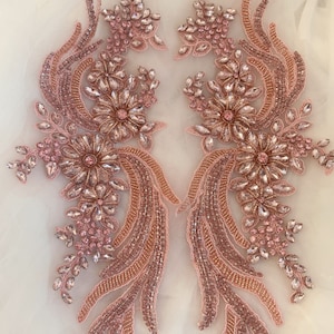 May include: Two rose gold beaded and sequined appliques with pink crystal embellishments. The appliques are shaped like a stylized bird with a floral design.