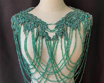 May include: A green beaded and jeweled shoulder piece with a leafy design. The piece is made of small, iridescent green beads and rhinestones.