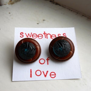 Puede incluir: Dos botones de madera marrón con un centro de vidrio azul. Los botones tienen un diseño floral y el texto "sweetness of love" está impreso en una tarjeta blanca detrás de ellos.