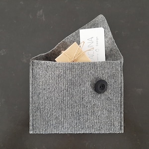 May include: A gray felt envelope with a black button closure. Inside the envelope is a small brown box tied with twine and a white card with the text "ACUNA Jewelry & Design".