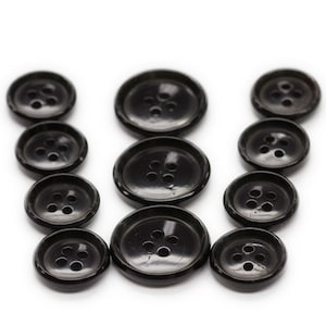 May include: A set of ten black plastic buttons of varying sizes, arranged in the shape of the letter "W".