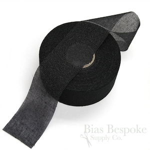 May include: A roll of black bias tape, a type of fabric used for finishing edges of garments. The tape is rolled up and a portion of the tape is unrolled, showing the texture of the fabric.