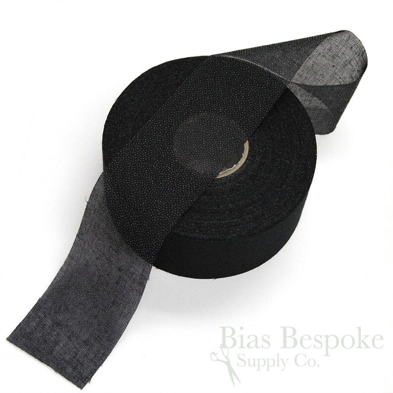 May include: A roll of black bias tape, a type of fabric used for finishing edges of garments. The tape is rolled up and a portion of the tape is unrolled, showing the texture of the fabric.