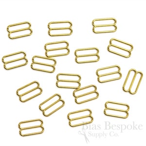 May include: A close-up of a pile of gold-colored metal slider buckles. The buckles are all the same size and shape, and they are arranged in a random pattern.