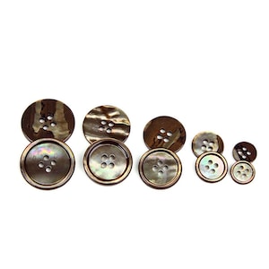 May include: Set of six brown and iridescent shell buttons with four holes each. The buttons are arranged in size order from largest to smallest.