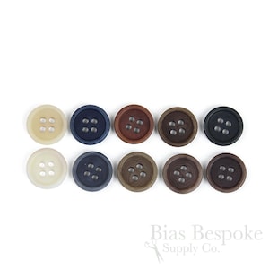 Puede incluir: Diez botones redondos de cuatro agujeros dispuestos en dos filas de cinco, con una variedad de colores que incluyen crema, azul, marrón y negro. El texto Bias Bespoke Supply Co. está impreso en la esquina inferior derecha.