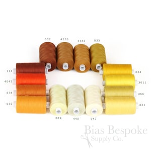 Peut inclure: Une collection de 12 bobines de fil de différentes nuances d'orange, de jaune et de beige. Les bobines sont disposées en cercle avec les numéros 114, 4045, 078, 030, 552, 4255, 2207, 035, 009, 445, 047, 034, 3011, 466 et 021 imprimés sur les bobines.