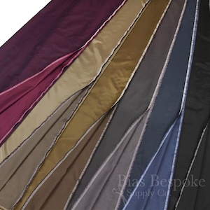 Puede incluir: Una colección de muestras de tela en varios tonos de marrón, gris y burdeos. La tela es una tafetán lisa y sedosa con un brillo sutil. Las muestras están dispuestas en forma de abanico, con el color más oscuro en la parte superior y el color más claro en la parte inferior.