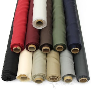May include: A collection of twelve fabric bolts arranged in two rows, featuring a variety of solid colors including black, red, burgundy, white, brown, olive green, navy blue, cream, tan, beige, light gray, and dark gray, with cardboard cores.