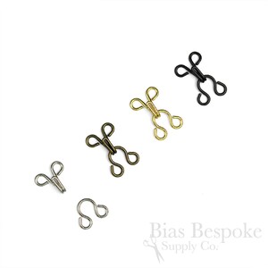 Peut inclure: Cinq fermoirs à crochet et à œil dans différentes finitions : argent, laiton antique, or et noir. Ils sont utilisés pour la couture et l’artisanat.