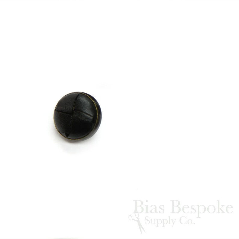 May include: A black leather button with a woven design. The button has a gold rim.