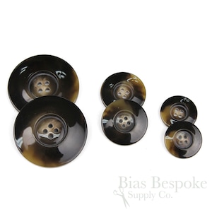 May include: Set of five brown and black horn buttons with four holes each. The buttons are different sizes and are arranged in a row from largest to smallest.