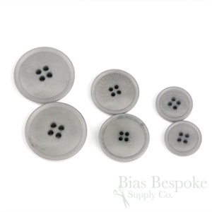 May include: Set of five gray plastic buttons with four holes each. The buttons are arranged in a size order from largest to smallest.