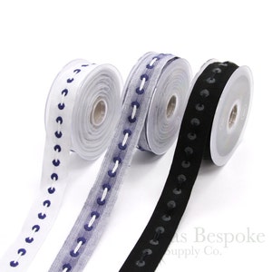 May include: Three spools of trim with a decorative stitch design. The trim is white, gray with blue stitching, and black. The spools are on a white background.