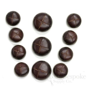 May include: Assortment of brown leather buttons with a cross stitch design. The buttons are various sizes.