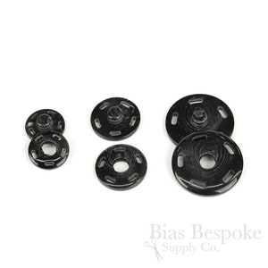 May include: A set of six black plastic snap fasteners in various sizes. The fasteners have a textured, wood-like finish.
