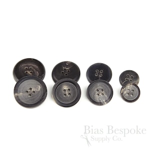May include: Set of six black and brown horn buttons with five holes each. The buttons are arranged in size order from largest to smallest.
