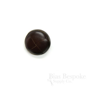 May include: A brown leather button with a stitched X pattern and a gold rim.