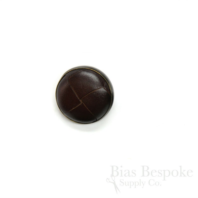 May include: A brown leather button with a stitched X pattern and a gold rim.