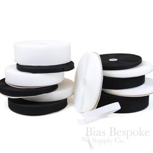 May include: Rolls of white and black hook and loop tape, also known as Velcro, are stacked on a white surface. The tape is a popular choice for crafts, sewing, and home decor projects.