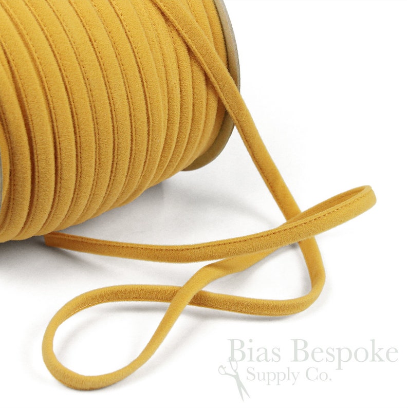 May include: A spool of mustard yellow velvet cord, with a length of the cord extending from the spool. The cord is soft and has a subtle sheen.