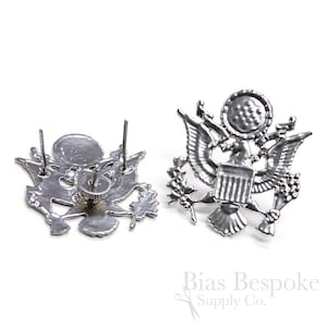 Puede incluir: Dos emblemas de sello presidencial de los Estados Unidos en metal plateado con cierre de tornillo. Los emblemas están detallados con un águila, un escudo y ramas de olivo.