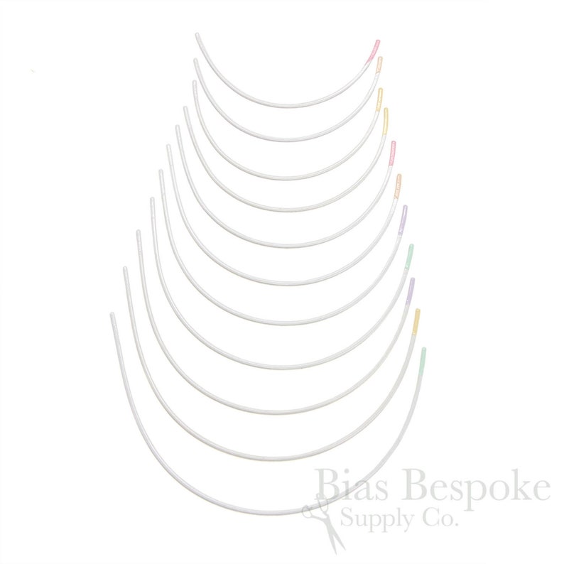 May include: A selection of white, curved bra underwires, fanned out. Some wires have coloured tips in pink, yellow, green, and purple. The background is plain white.