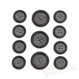 May include: Set of ten black plastic buttons with five holes each. The buttons are arranged in three rows, with the largest buttons at the top and the smallest buttons at the bottom.
