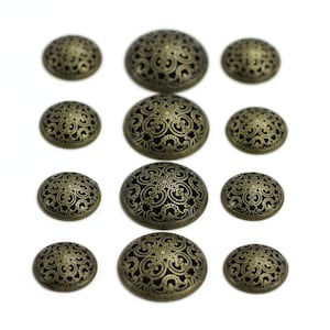 May include: Assortment of 10 round, decorative buttons with a black and gold finish. The buttons have a filigree design and are arranged in three rows.