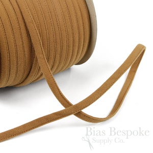May include: A spool of brown cord or ribbon with a soft, suede-like texture. The cord is approximately 1/4 inch wide and is wound around a cardboard spool.