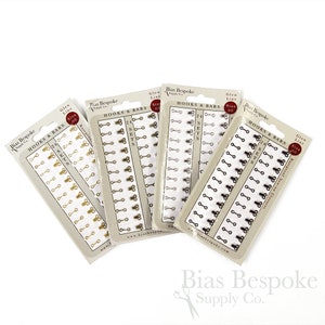 May include: Four packages of hooks and bars for sewing. Each package contains 24 sets of hooks and bars in gold, silver, bronze, and black.