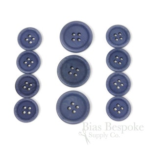 Può includere: Un set di dieci bottoni in plastica blu, ognuno con quattro fori. I bottoni sono disposti in tre file, con i bottoni più grandi nella fila centrale.