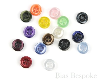 Könnte beinhalten: Sortiment von 15 bunten Kunststoffknöpfen mit jeweils vier Löchern. Die Knöpfe sind in verschiedenen Farben, darunter Rot, Orange, Gelb, Grün, Blau, Lila, Schwarz, Weiß und Braun.