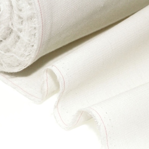 Puede incluir: Primer plano de un rollo de tela blanca con un hilo rosa que recorre el borde. La tela es suave y tiene una textura sutil.