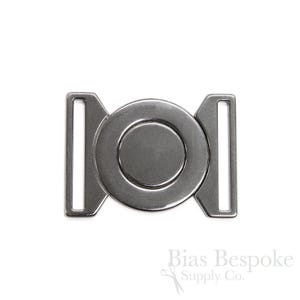 Pode incluir: Fivela de metal prateado com um design redondo de círculos concêntricos. A fivela é projetada para ser usada com um cinto ou uma correia.