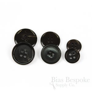Op de afbeelding: Vier zwarte hoornknoppen in verschillende maten. De knoppen hebben elk vijf gaten.
