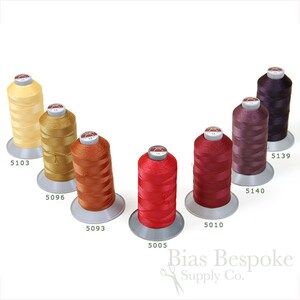 May include: Seven spools of thread in various shades of red, orange, yellow, and purple. The spools are arranged in a semi-circle with the numbers 5103, 5096, 5093, 5005, 5010, 5140, and 5139 printed below each spool.