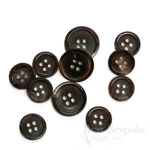 May include: A collection of ten brown horn buttons with four holes each. The buttons are arranged in a random pattern on a white background.