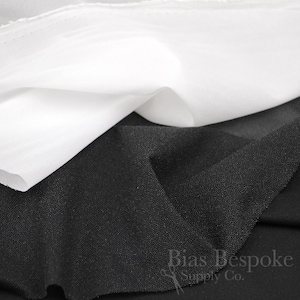 May include: A piece of white fabric layered over a piece of black fabric with a textured surface. The black fabric features the text Bias Bespoke Supply Co. with a small scissors icon printed in the bottom right corner of the image.