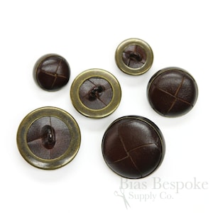 May include: Five brown leather buttons with a gold metal rim. The buttons have a stitched X pattern on the leather.