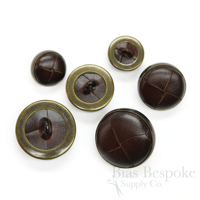 May include: Five brown leather buttons with a gold metal rim. The buttons have a stitched X pattern on the leather.