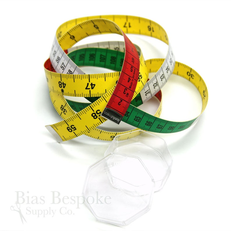 May include: A coiled measuring tape in yellow, red, green, and white, with black measurement markings. The tape is marked in inches and centimeters. Two clear, hexagonal plastic containers are in the foreground. The image is on a white background.
