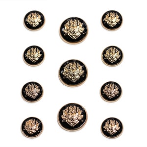 Puede incluir: Diez botones negros y dorados con un diseño decorativo. Los botones tienen un diseño dorado en relieve sobre un fondo negro.