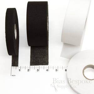 May include: Three rolls of black and white bias tape, each measuring 1 inch wide. The tape is shown on a white surface with a ruler for scale. The ruler is marked in inches.