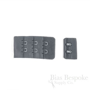 May include: A grey bra extender featuring three columns of hook-and-eye closures on a fabric strip, accompanied by a smaller matching fabric piece with two eye loops. The text Bias Bespoke Supply Co. is visible in the bottom right corner.