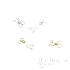 May include: Five metal hook and eye closures in two colors: white and gold. The closures are used for sewing garments.