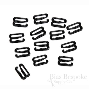 May include: A close-up of 14 black plastic bra strap adjusters. The adjusters are in the shape of an 'S' and have two loops on each side.
