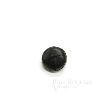 May include: Black leather button with a stitched cross pattern and a gold metal rim.